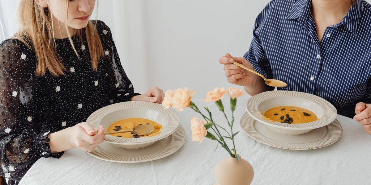 Two women enjoying homemade pumpkin soup at a dining table with floral decor.