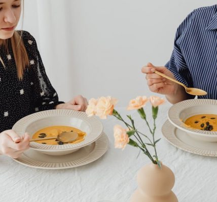 Two women enjoying homemade pumpkin soup at a dining table with floral decor.