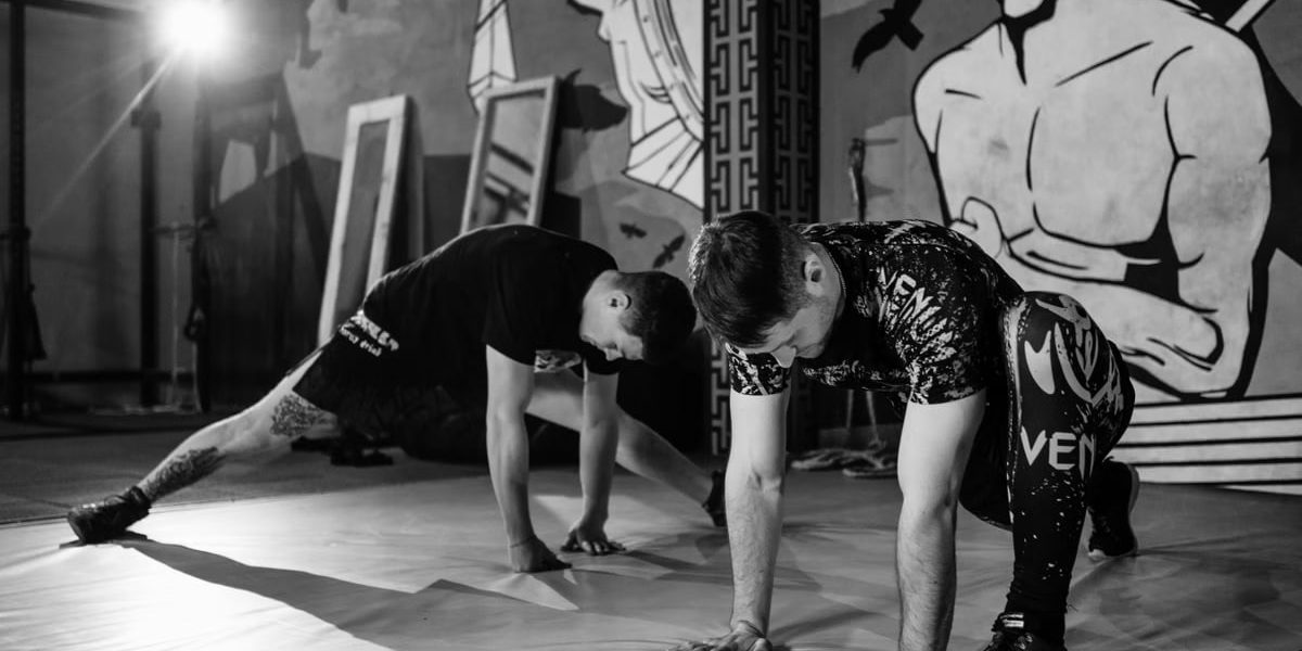 Two men stretching inside a gym, preparing for MMA training in a grayscale setting.