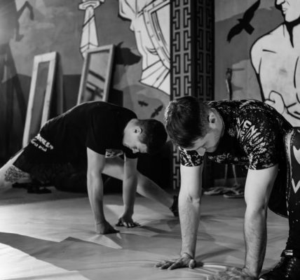 Two men stretching inside a gym, preparing for MMA training in a grayscale setting.